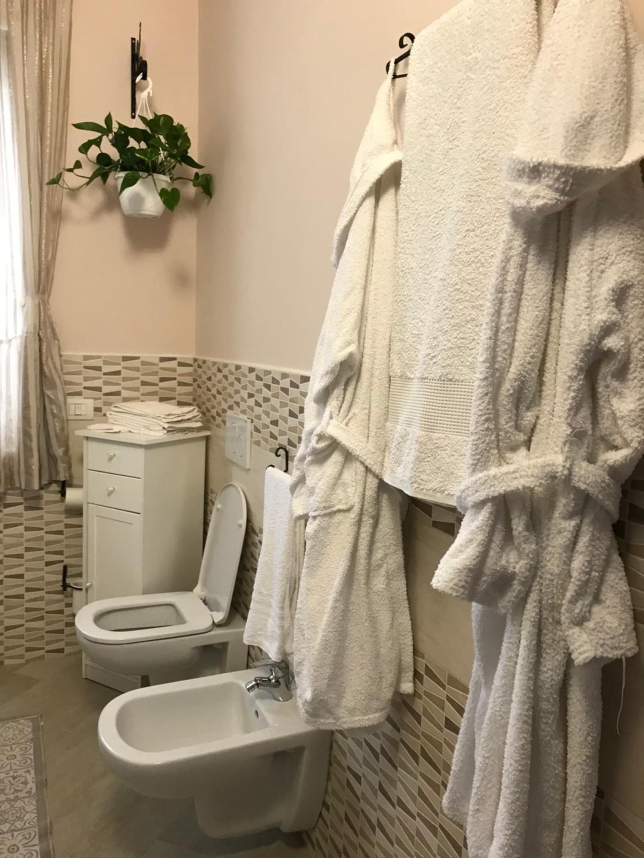 Un baño con inodoro, bidé y un perchero con bata blanca.