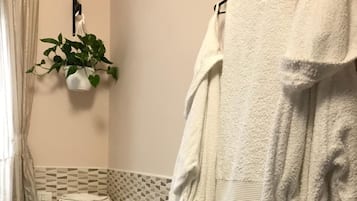 Un baño con inodoro, bidé y un perchero con bata blanca.