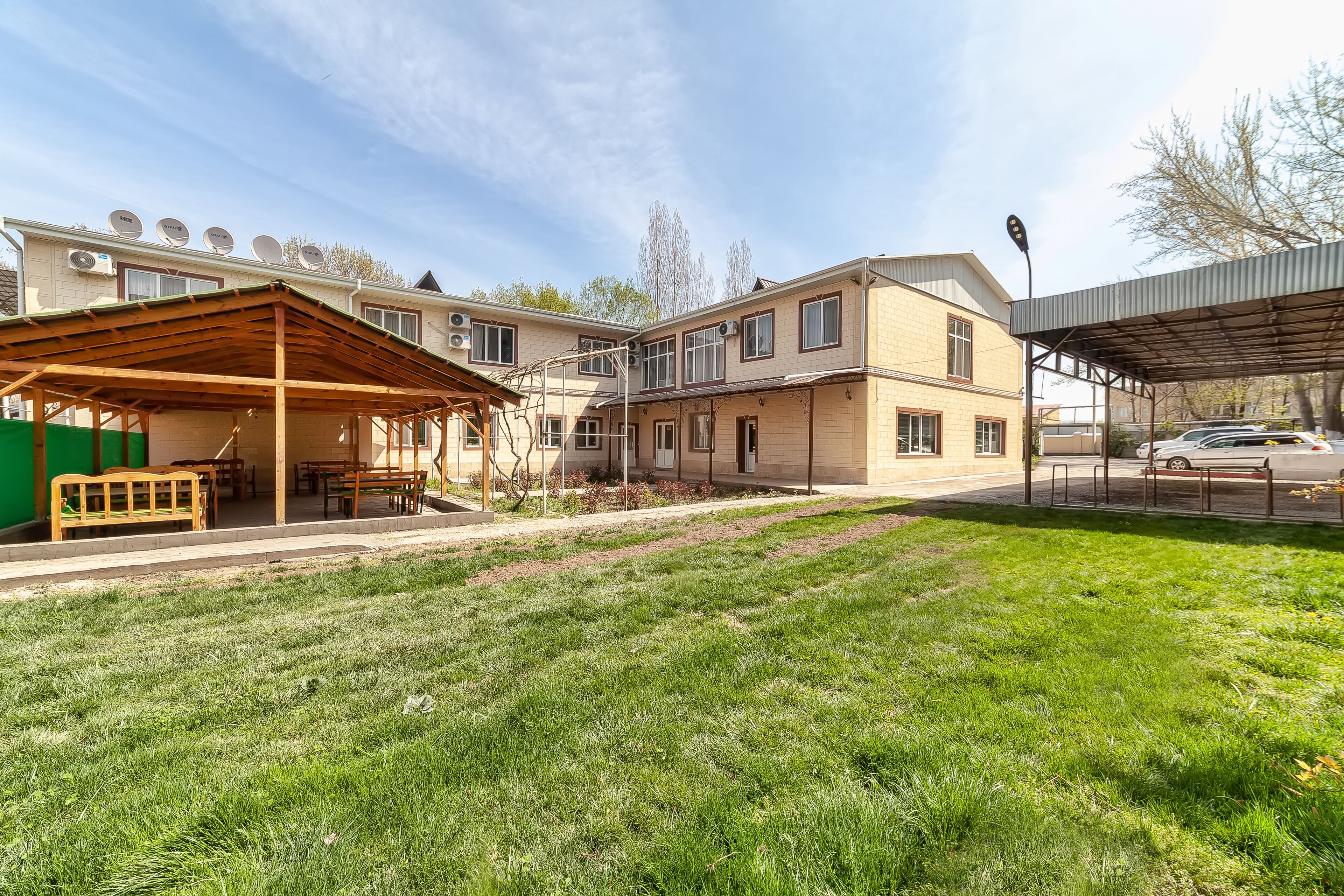 A residential building with multiple satellite dishes, a covered outdoor area with benches, and a well-maintained lawn.