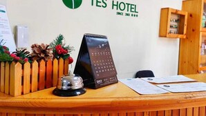 Una recepción de hotel con un mostrador de madera, un calendario, una campana y un letrero que dice "TES HOTEL SINCE 2003".