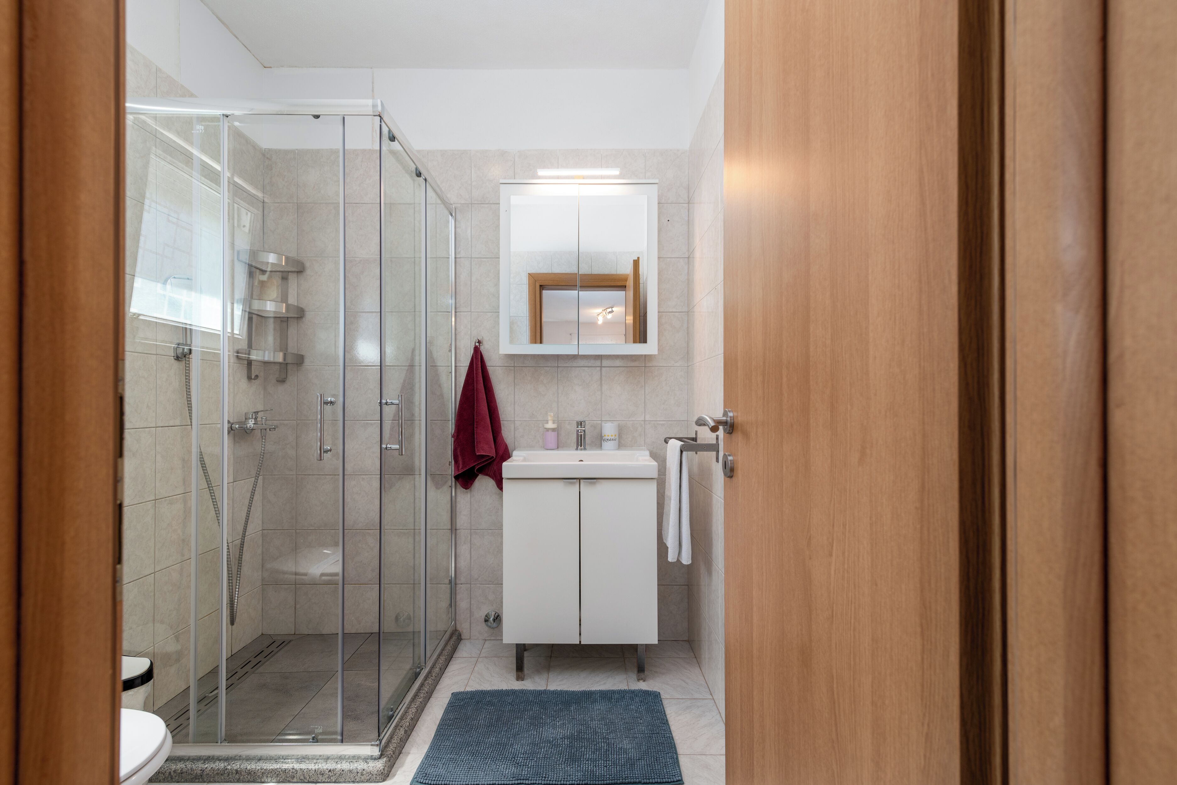 A modern bathroom with a glass-enclosed shower, a white sink, and a wooden door.