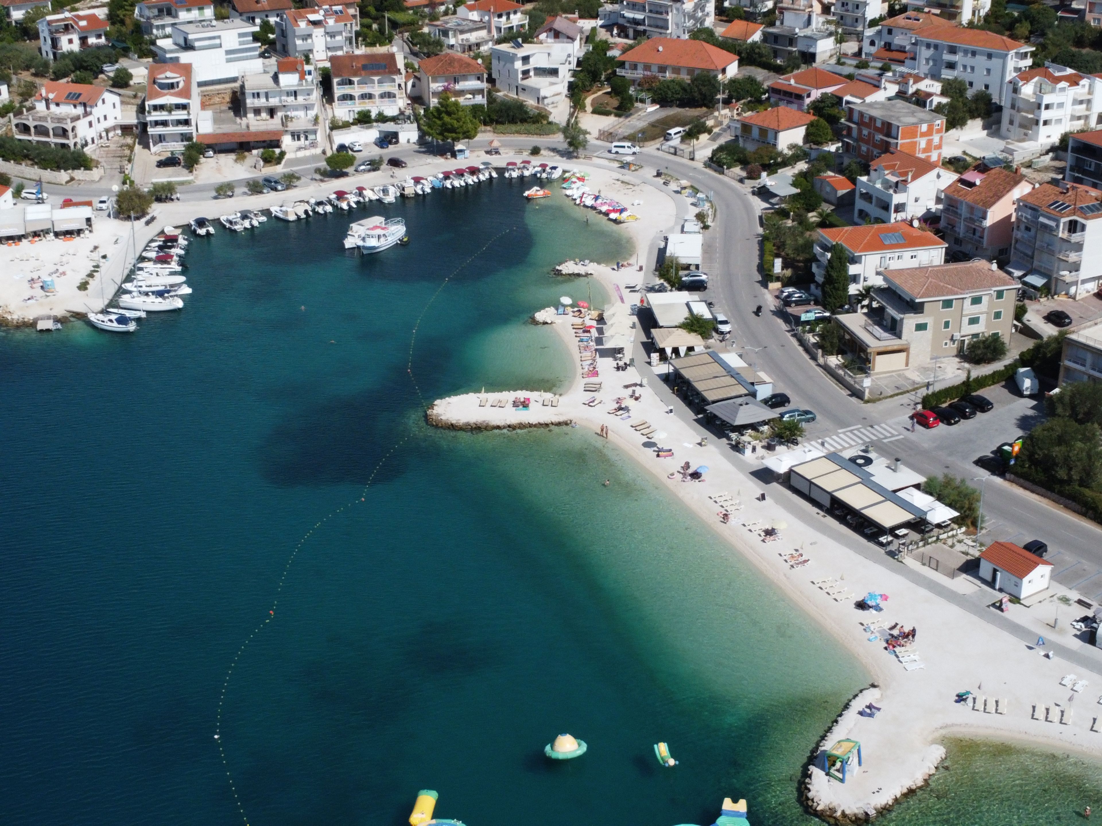Luftaufnahme einer Küstenstadt mit einem Yachthafen, Strand und Wohnhäusern.