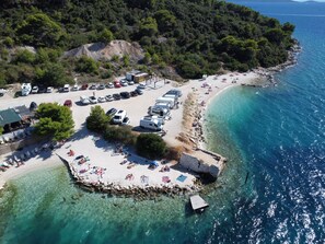 An aerial view of a coastal area with a beach, parked vehicles, and a small dock. - Villa Eight by A (Okrug)