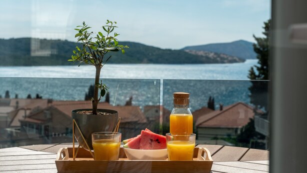 A table with a tray containing a glass of orange juice, a glass of water, a bowl of watermelon, and a bottle of orange juice. A small potted plant is also on the tray. - Villa Eight by A (Okrug)