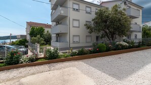 A multi-story residential building with balconies, a gravel driveway, and a fenced garden area with flowers. - Villa Eight by A (Okrug)