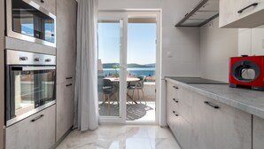 A modern kitchen with a sliding glass door leading to a balcony with a view of the sea. - Villa Eight by A (Okrug)