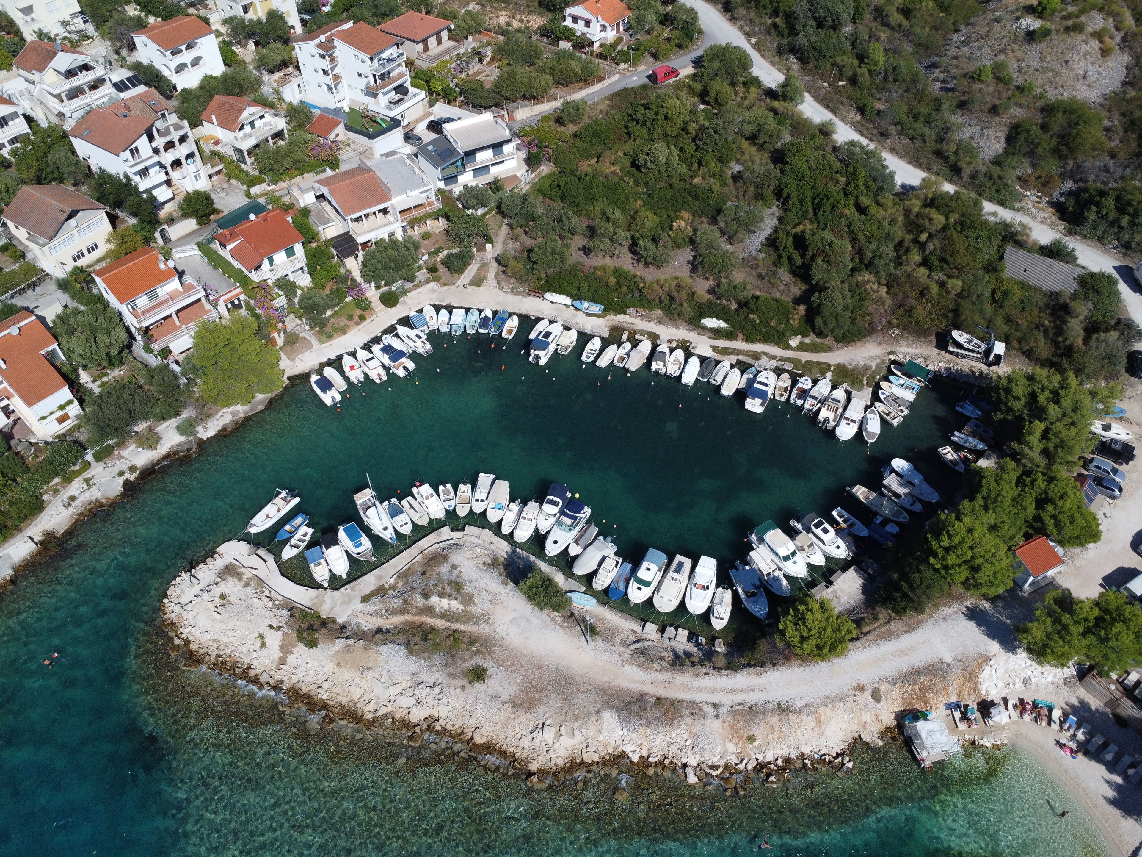 An aerial view of a marina with boats docked in a circular arrangement, surrounded by residential buildings and greenery.