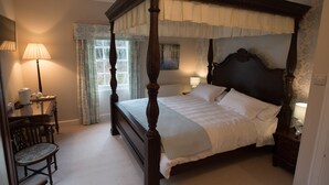 A four-poster bed with a canopy, a bedside table with a lamp, a chair, and a window with curtains. - Elibank House B&B (Walkerburn)