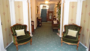 A hallway with two green armchairs, a staircase, and a chandelier. - Elibank House B&B (Walkerburn)