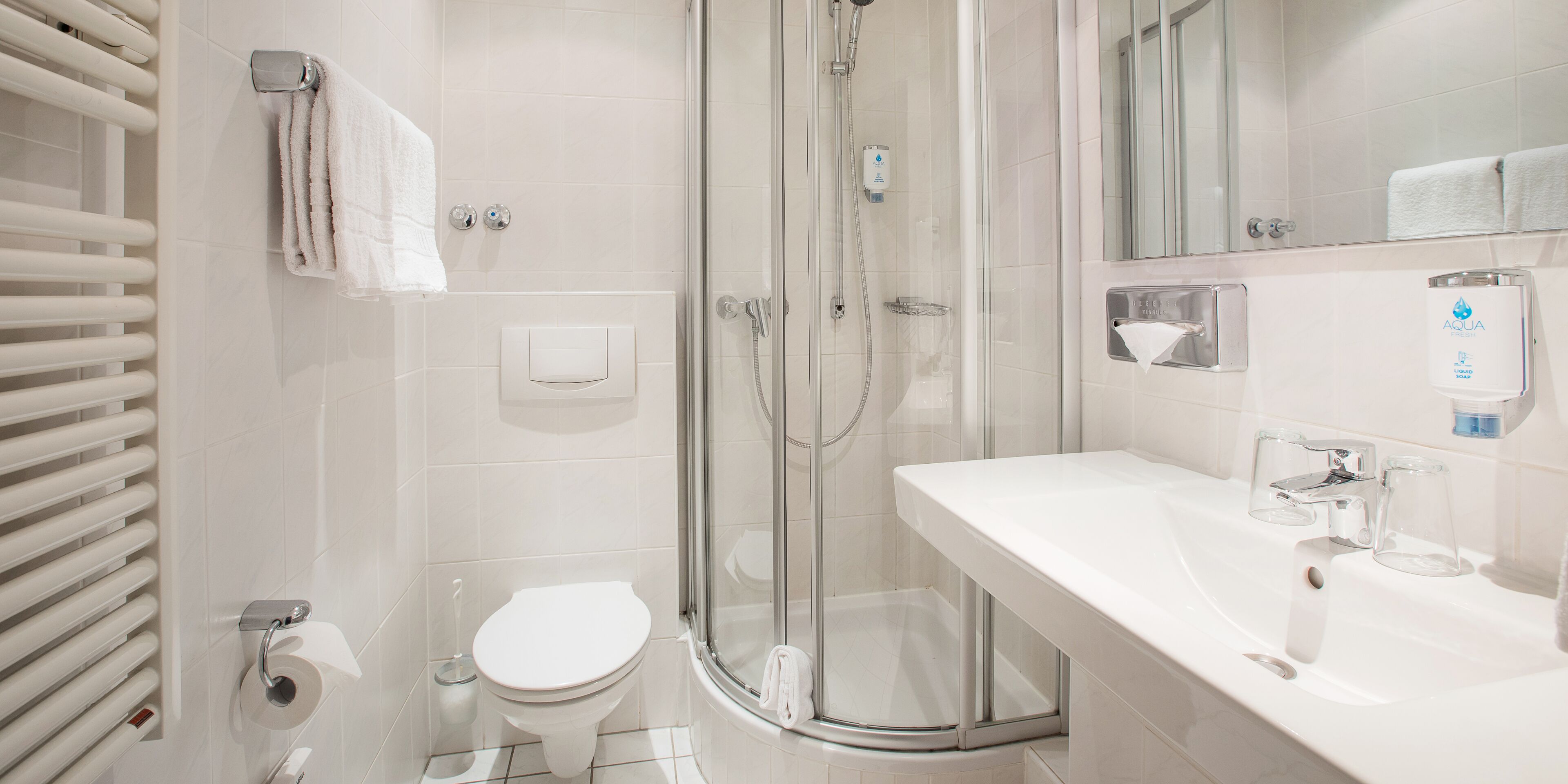 Un baño moderno con ducha envuelta en vidrio, inodoro blanco y lavamanos con espejo.
