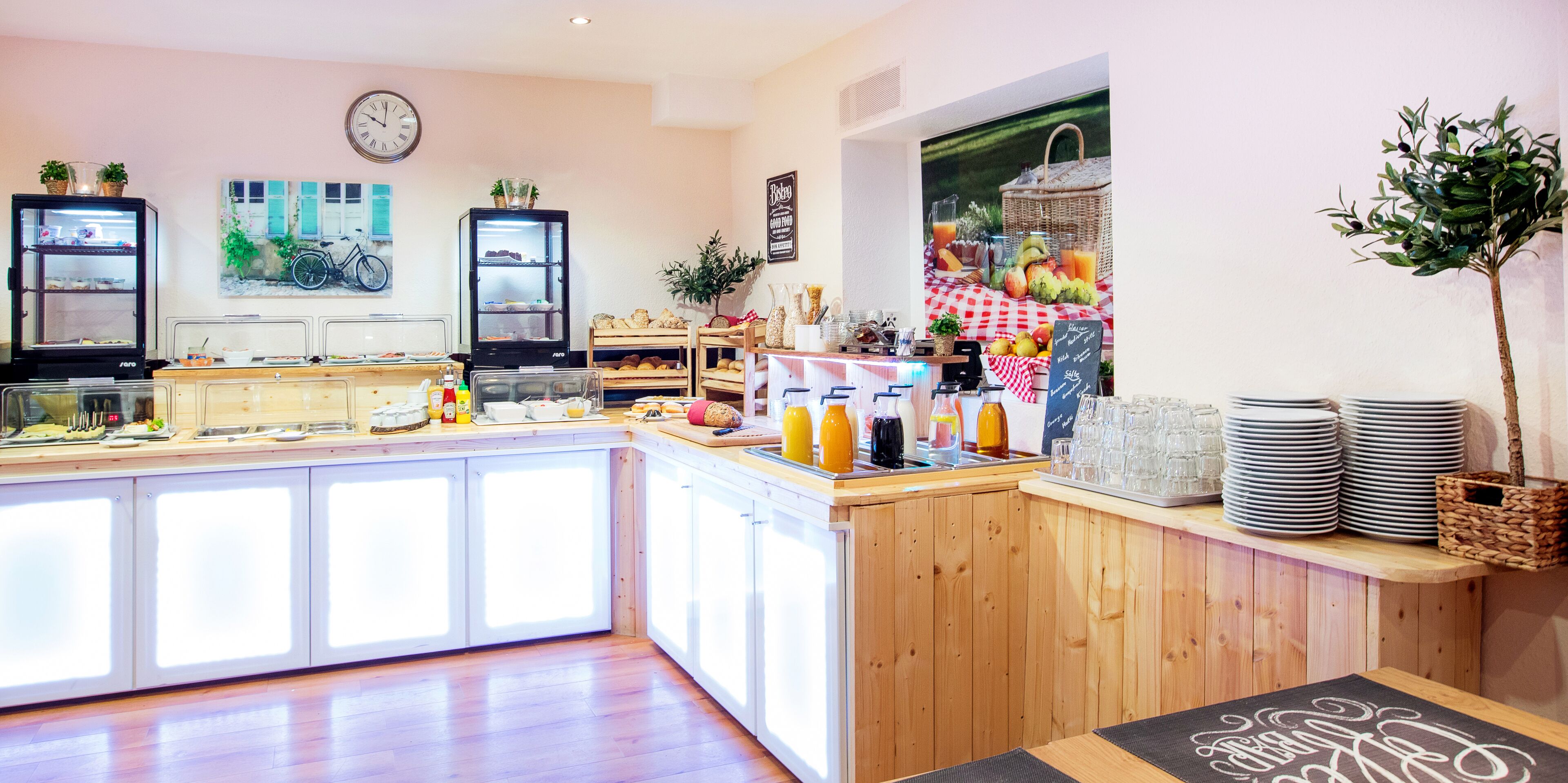 A breakfast bar with a clock, a refrigerator, and a fruit display.
