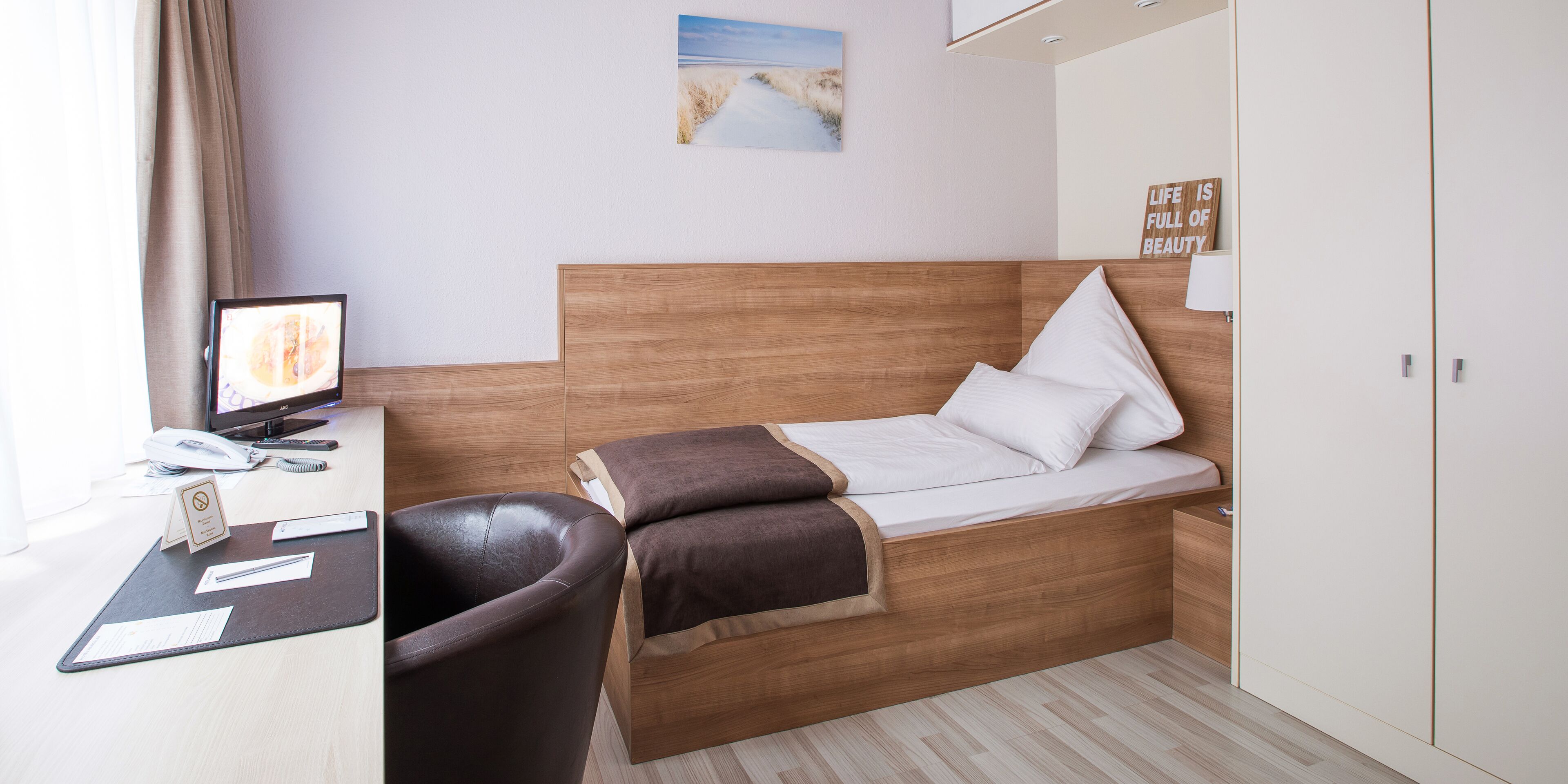 Habitació d'hotel ben ordenada amb un llit de fusta, un escriptori amb un ordinador i una cadira.