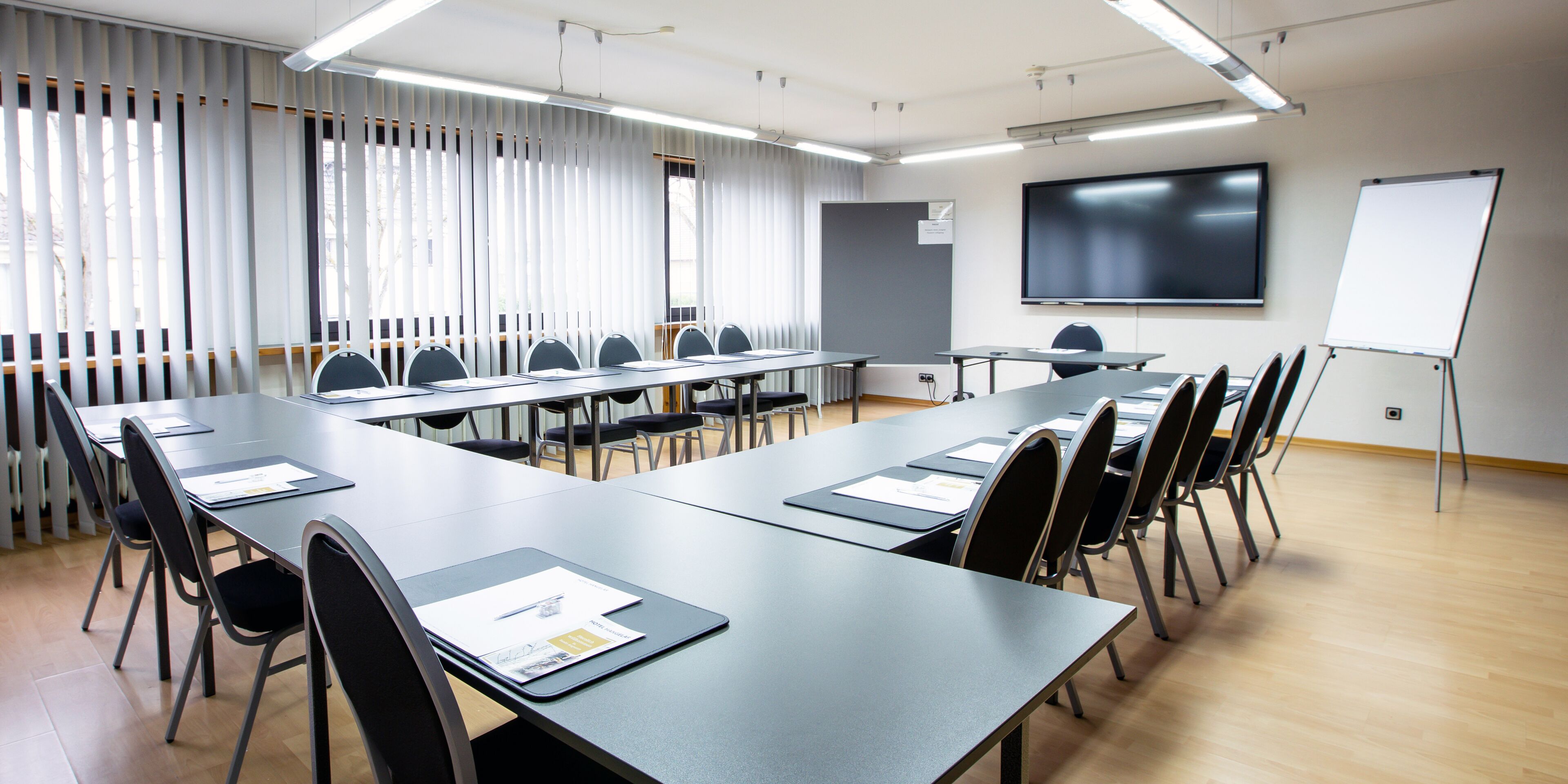 Un salón de conferencias con una mesa larga, sillas, una pizarra y una pantalla de proyector.