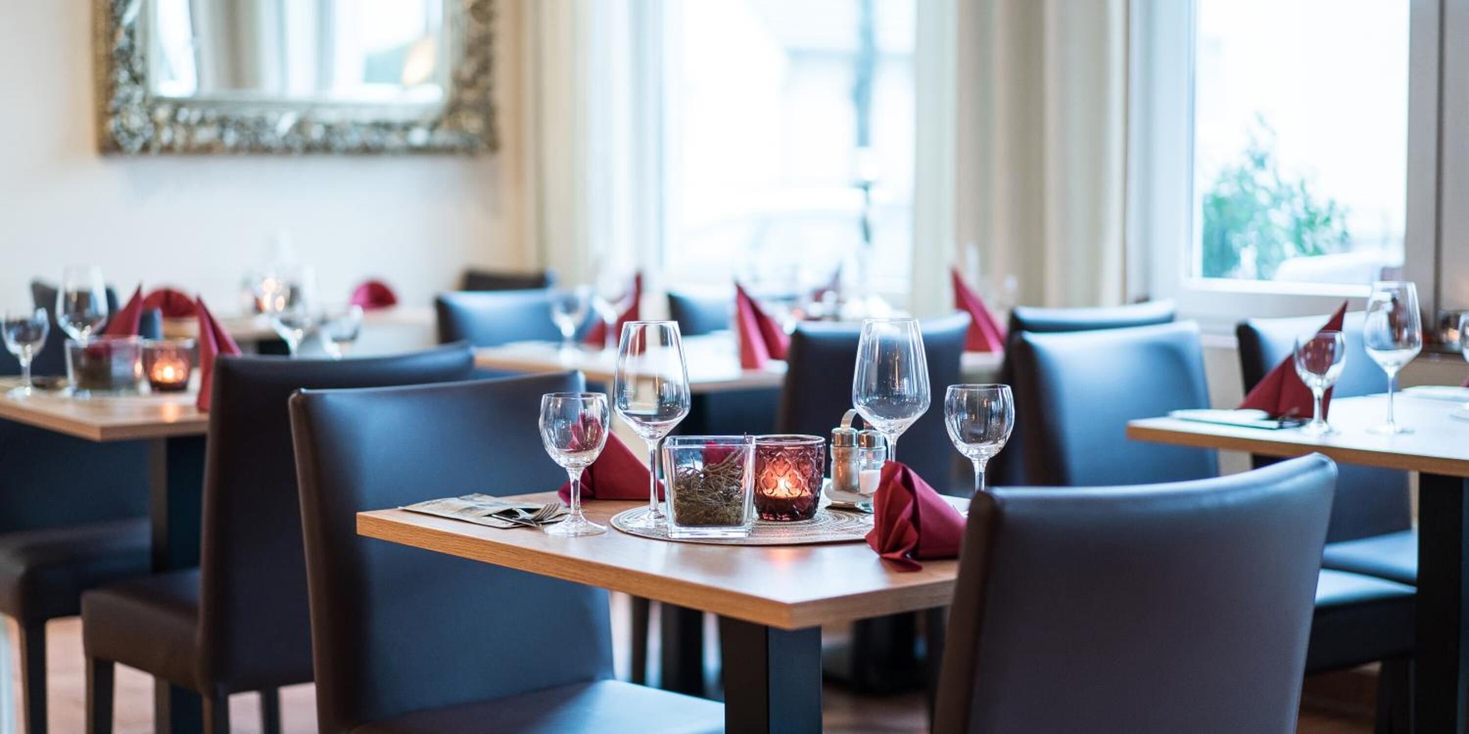 A restaurant interior with tables set for dining, featuring clear glassware and red napkins.
