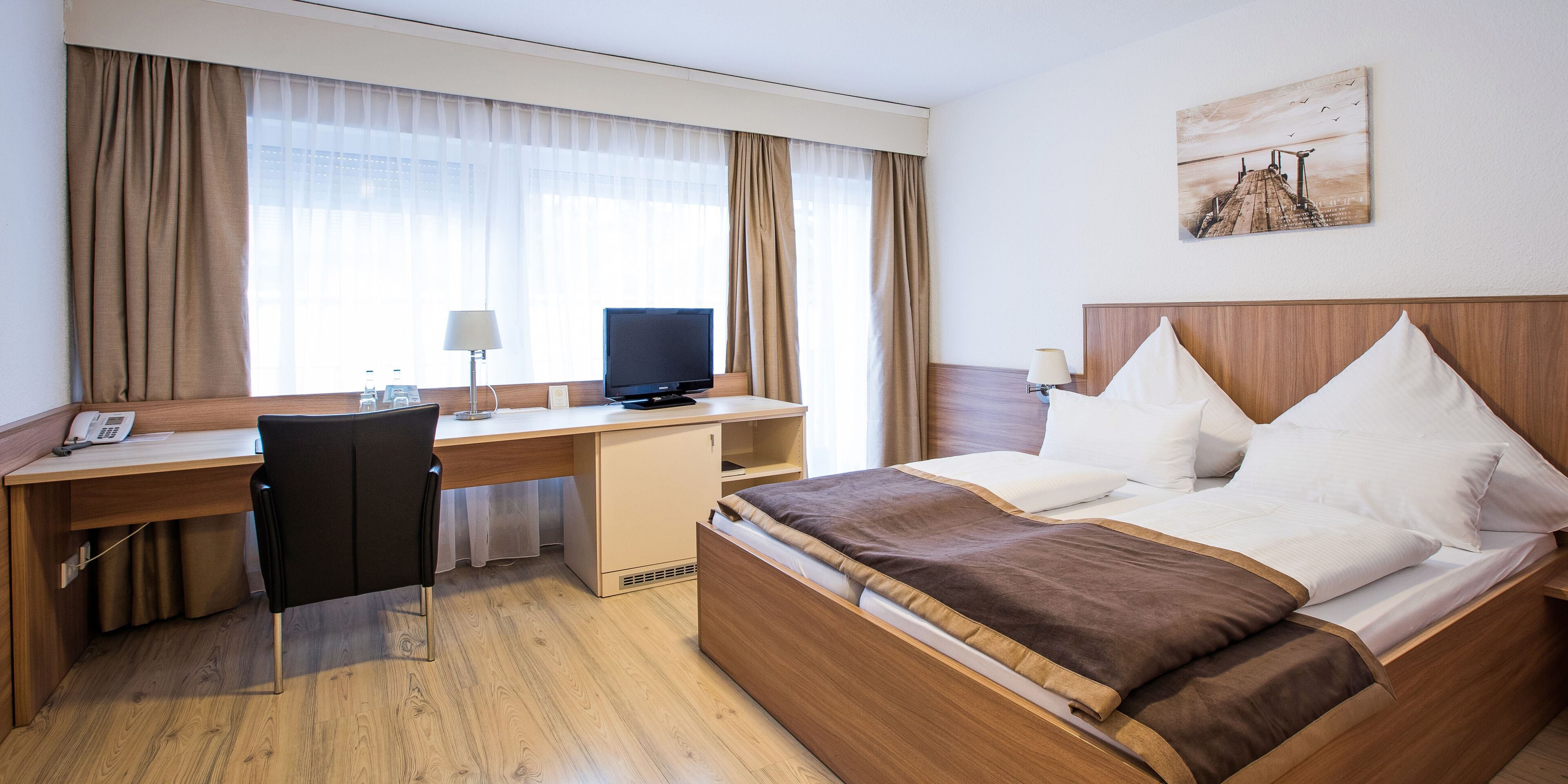 Ein Hotelzimmer mit Bett, Schreibtisch, Stuhl, Fernseher und einem Bild an der Wand.