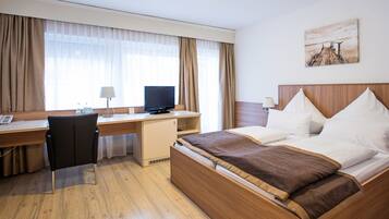 Ein Hotelzimmer mit Bett, Schreibtisch, Stuhl, Fernseher und einem Bild an der Wand.