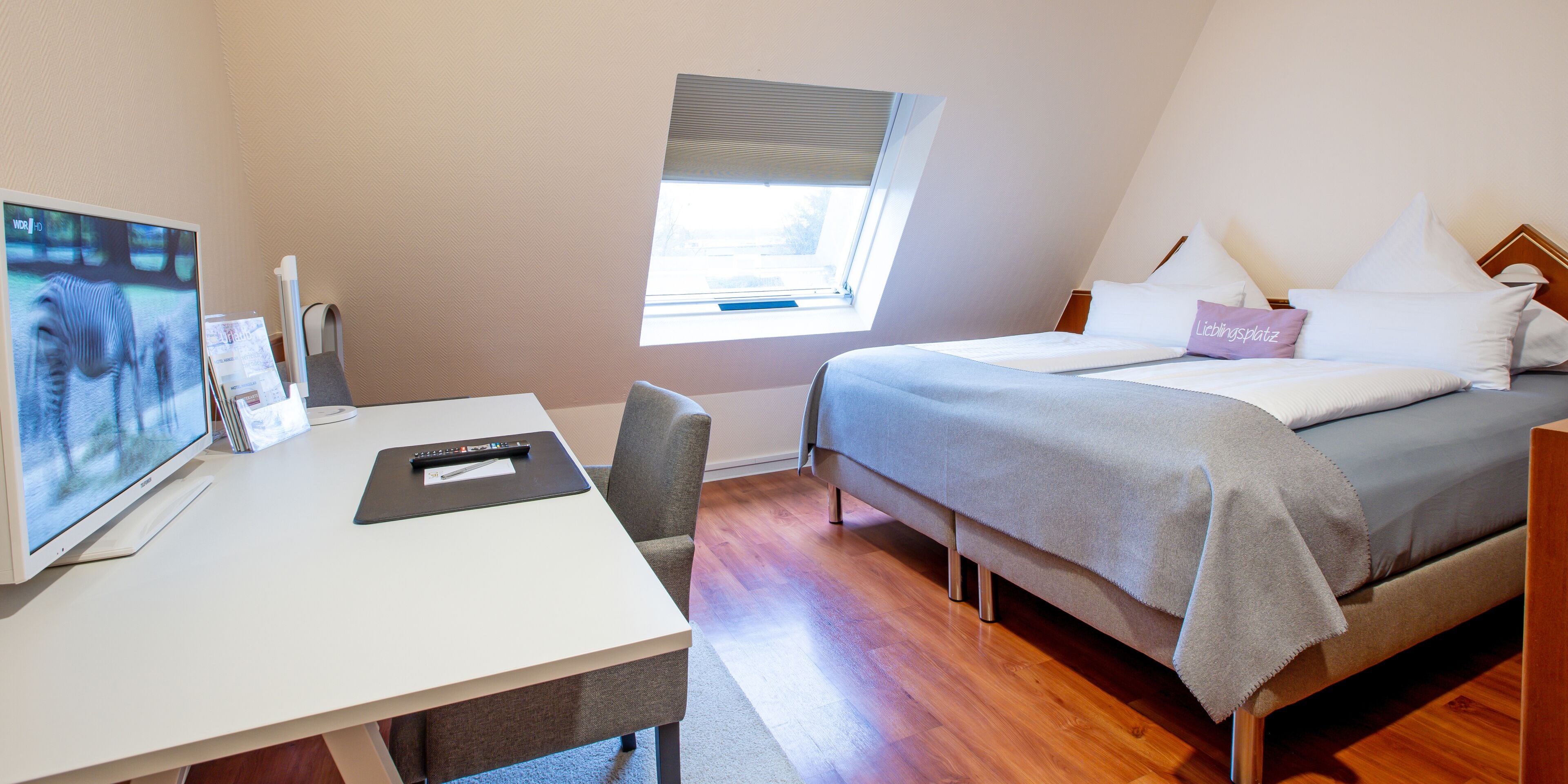 A hotel room with a bed, a desk with a computer, a window, and a view of the outdoors.