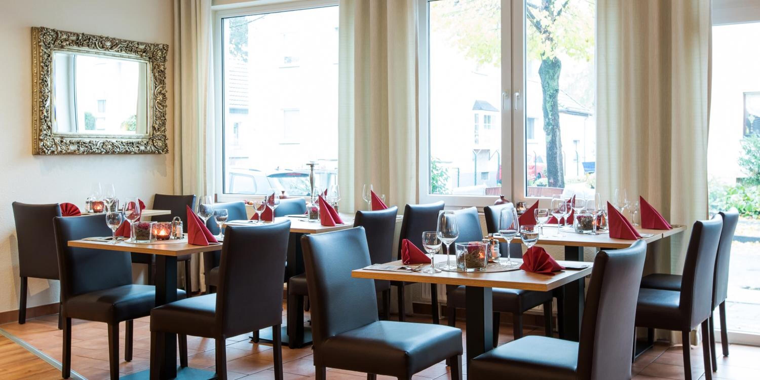 Restaurante com mesas postas para refeições, cadeiras e uma grande janela com vista para a rua.