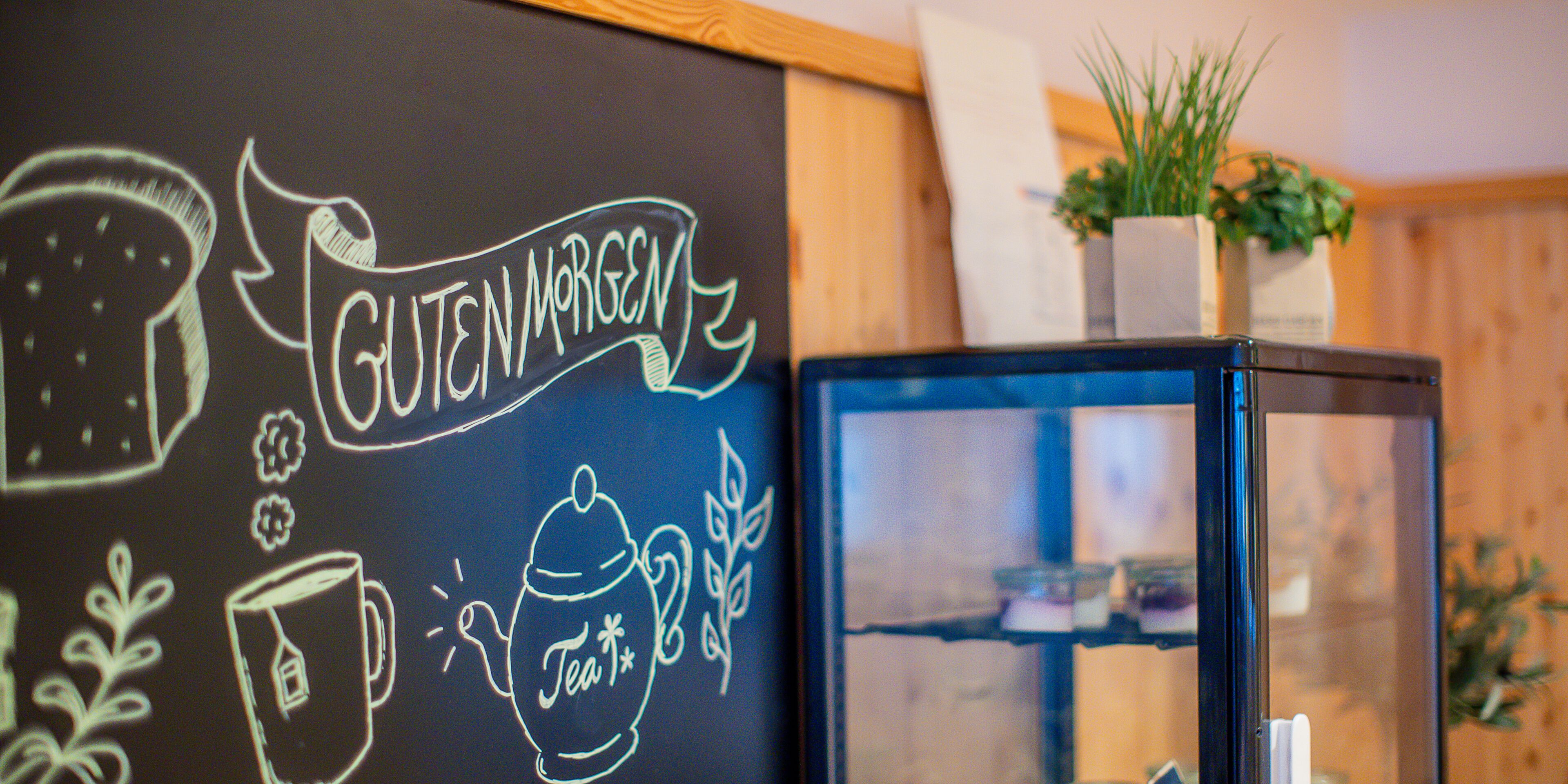 Een schoolbord met tekeningen van een theepot en kopje, en de tekst 'Guten Morgen'.