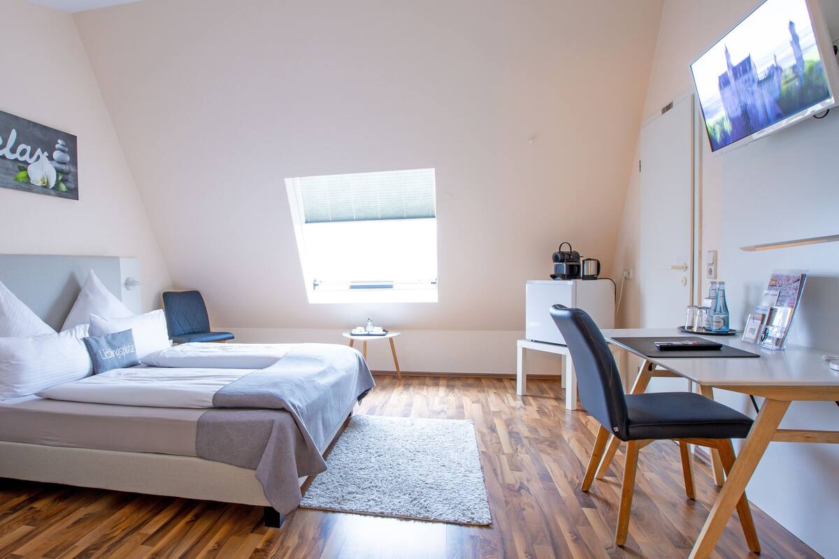 A modern bedroom with a bed, a desk, a chair, a TV, and a window.