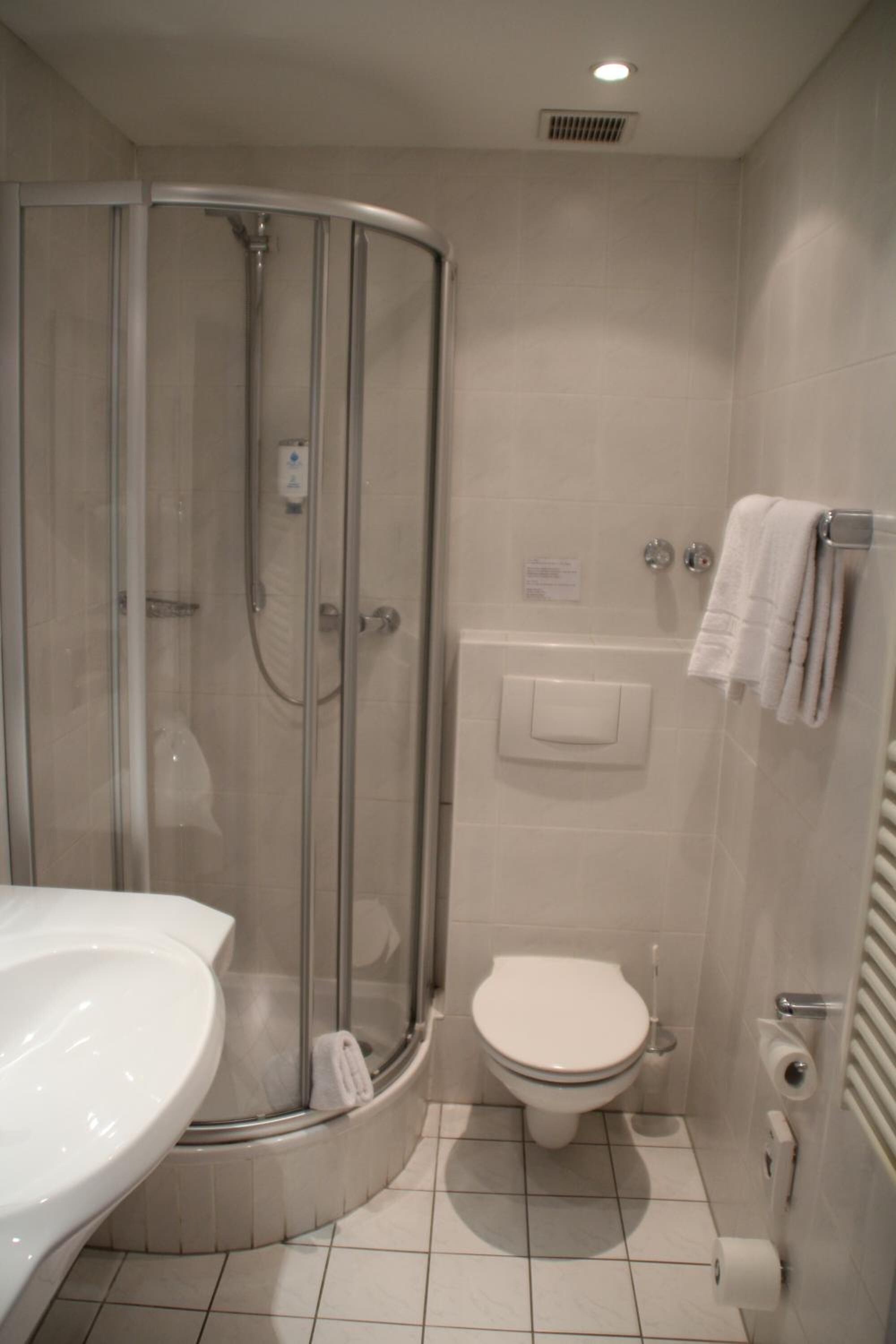 A bathroom with a glass-enclosed shower, a toilet, a sink, and a towel rack.