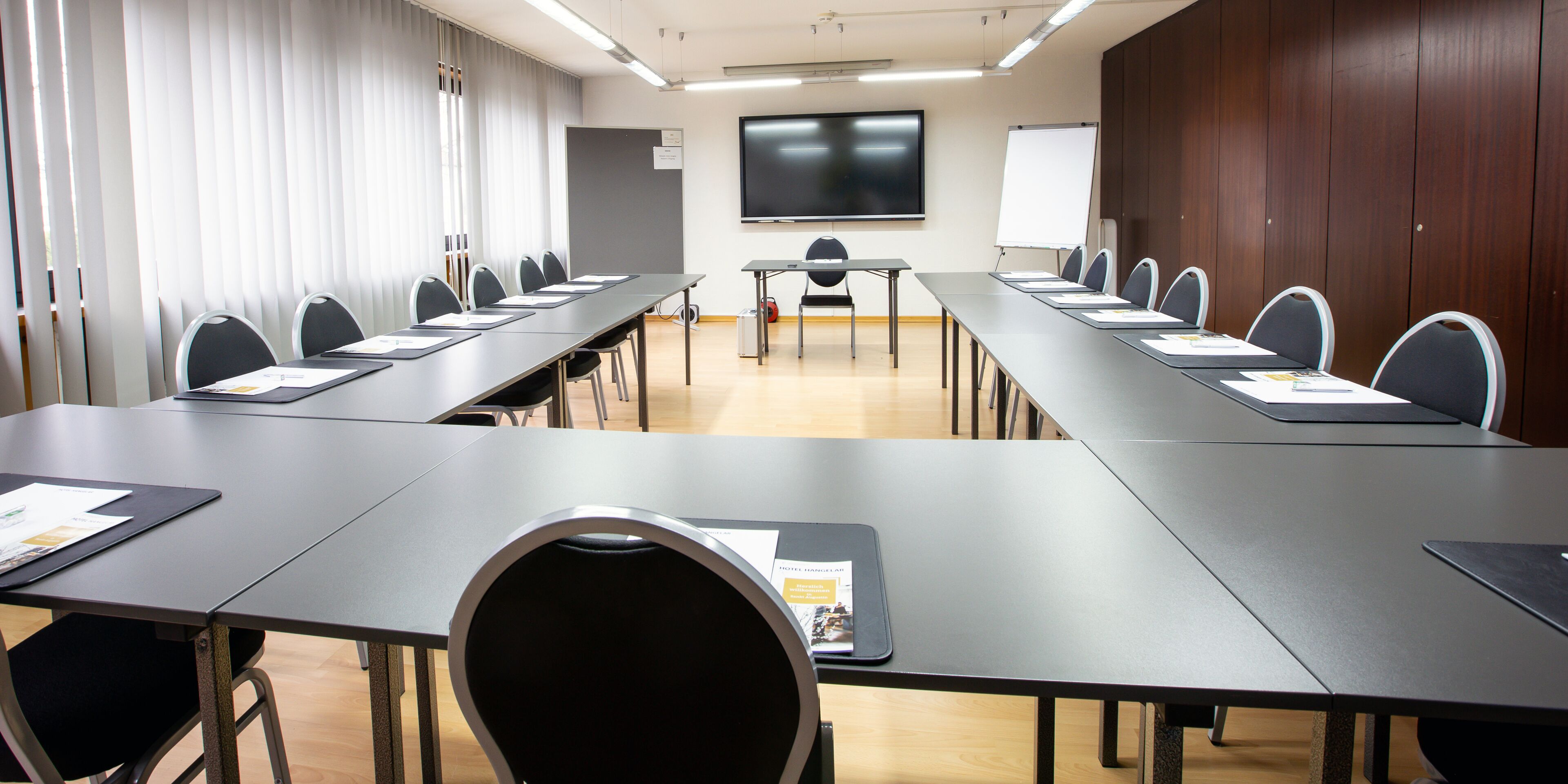 Een vergaderruimte met een lange tafel, stoelen, een projectiescherm en een whiteboard.