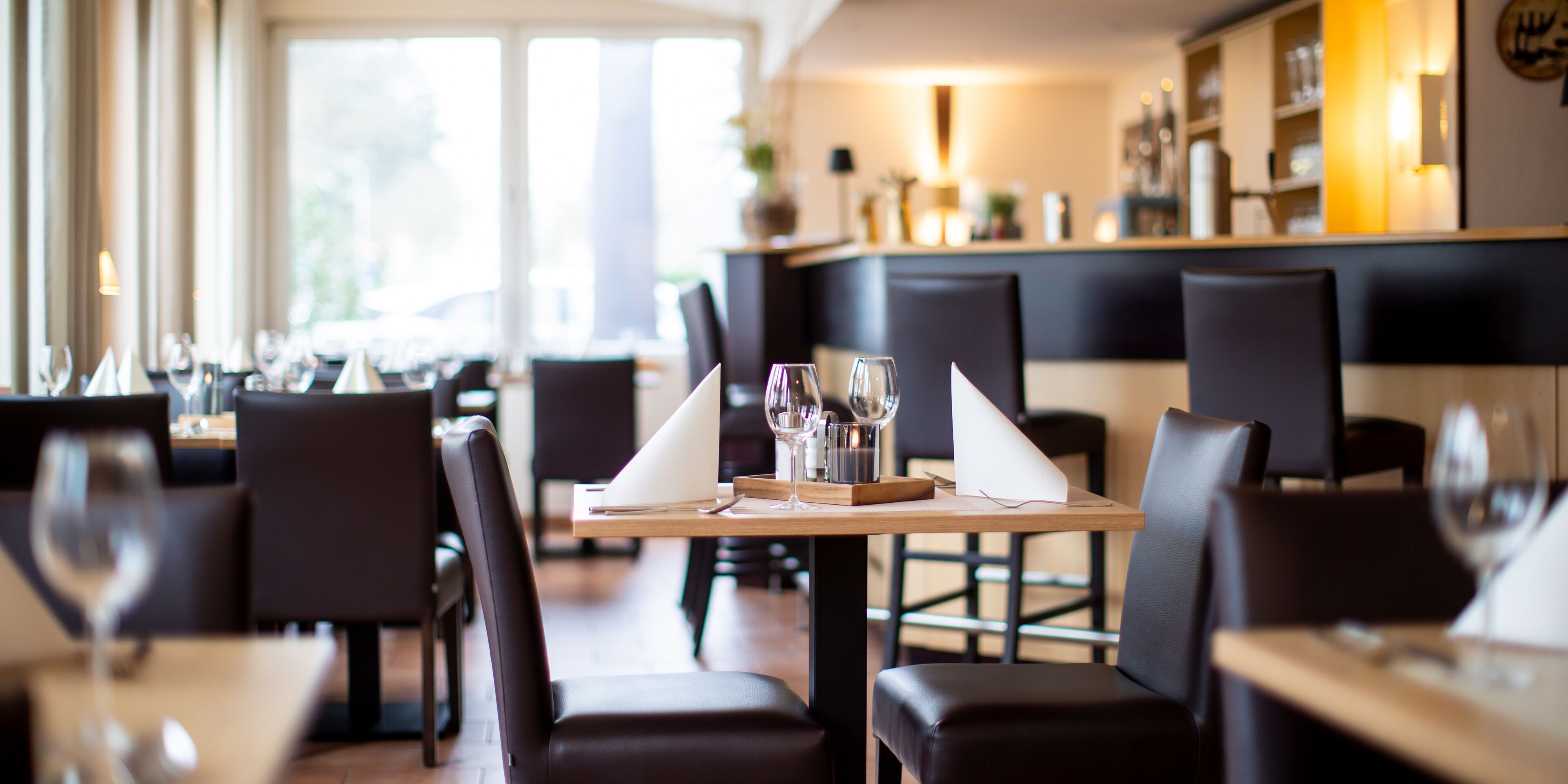Un interior de restaurante con mesas dispuestas para comer, sillas y una zona de bar al fondo.