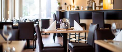 Un interior de restaurante con mesas dispuestas para comer, sillas y una zona de bar al fondo.
