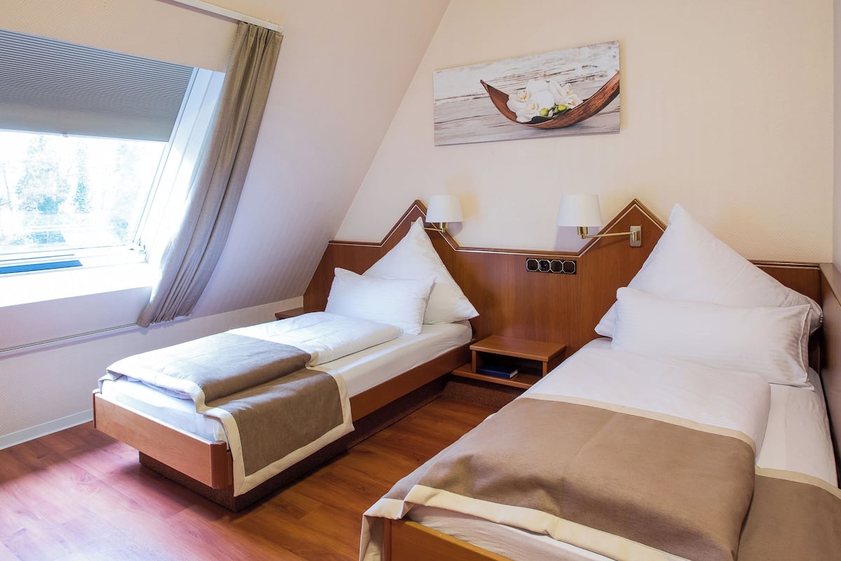 A hotel room with a large window, a bed with a wooden headboard, a bedside table, and a wall-mounted lamp.