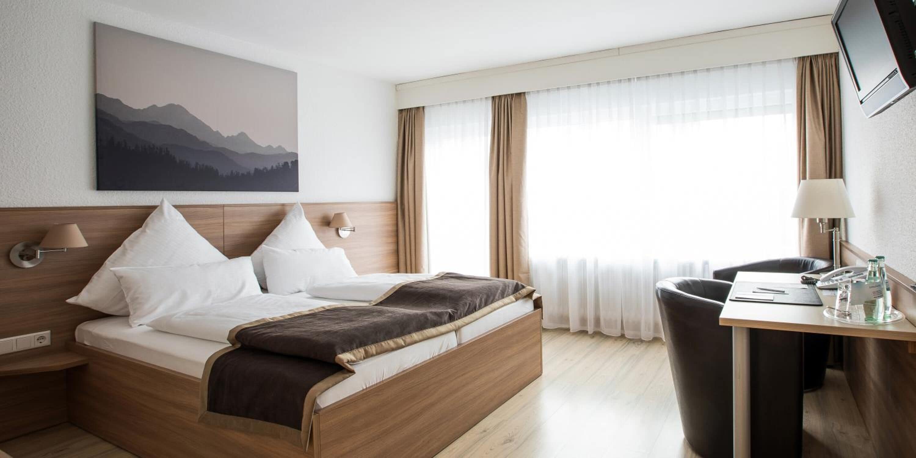 Hotellihuone, jossa on sänky, työpöytä, tuoli, televisio ja ikkuna, jossa on verhot.