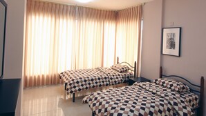 Habitación de hotel con dos camas, un ventanal con cortinas, un cuadro en la pared y un televisor de pantalla plana.