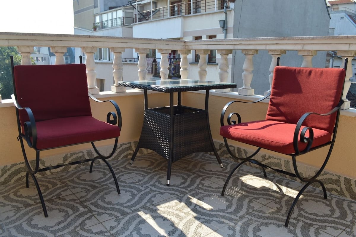 A balcony with two red chairs and a small table.