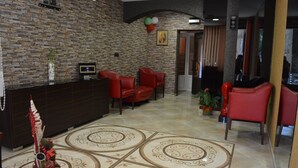 A reception area with a stone wall, red chairs, a dark wooden desk, and a tiled floor with a decorative pattern. - Bon Bon Hotel (Sofia)