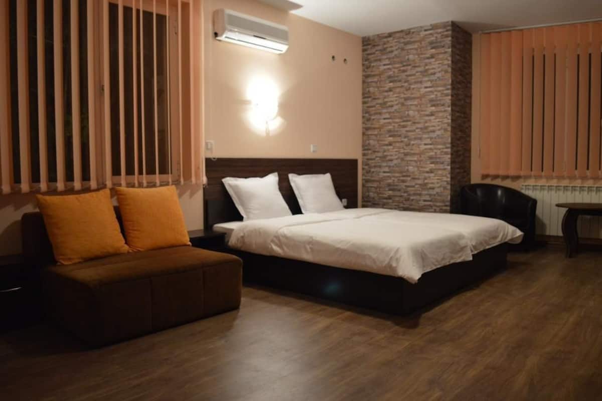 A hotel room with a bed, a sofa, a desk, and a stone accent wall.
