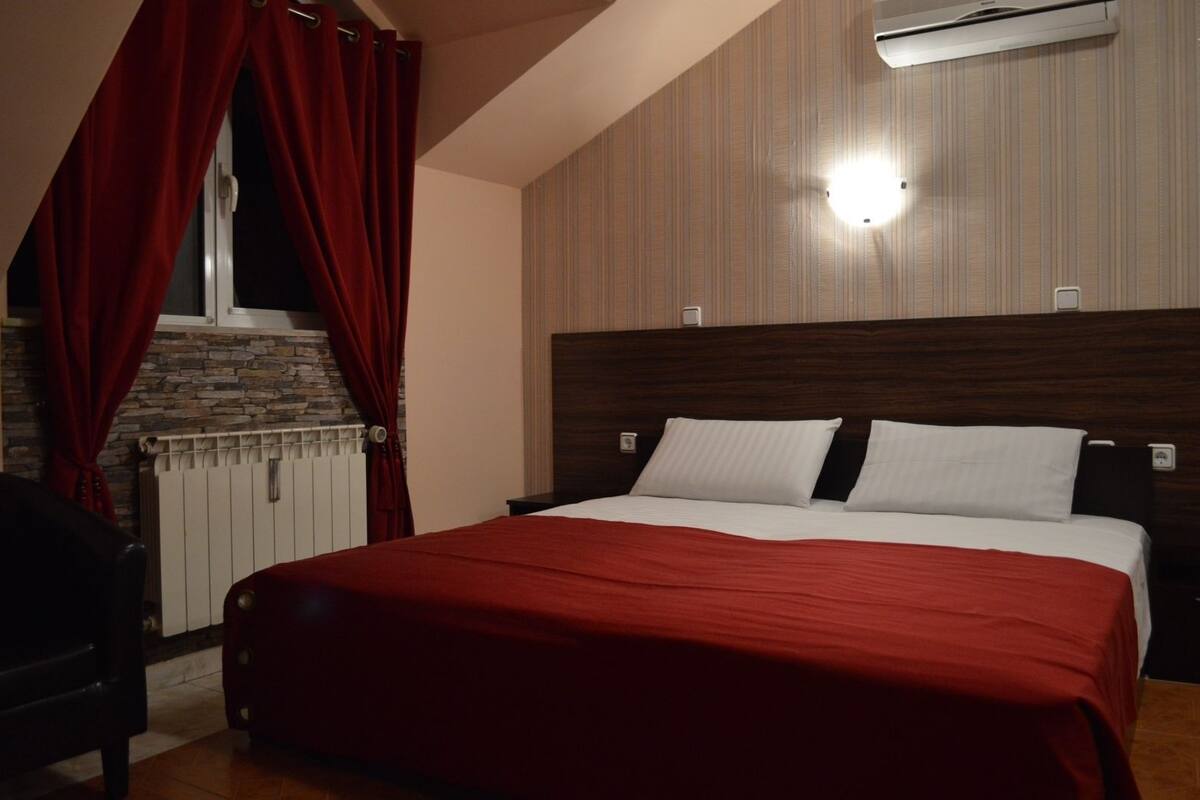 A bedroom with a bed, red curtains, a stone fireplace, and an air conditioning unit.