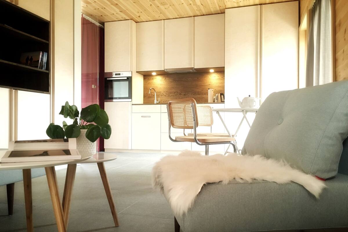 Een moderne woonkamer met een grijze bank, een witte, pluizige plaid, een houten salontafel en een rieten fauteuil.