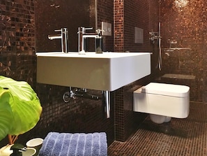 A bathroom with a white sink, chrome faucets, a white toilet, and a tiled wall.