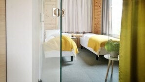Ett modernt hotellrum med träinredning, en säng, ett sängbord, en växt och ett fönster med gardiner.