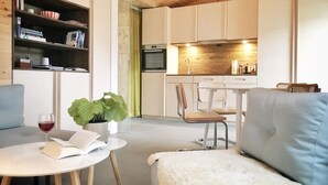 Ett modernt vardagsrum med en soffa, ett runt bord med en bok och ett glas vin, en bokhylla och en köksdel med ett matbord och stolar.