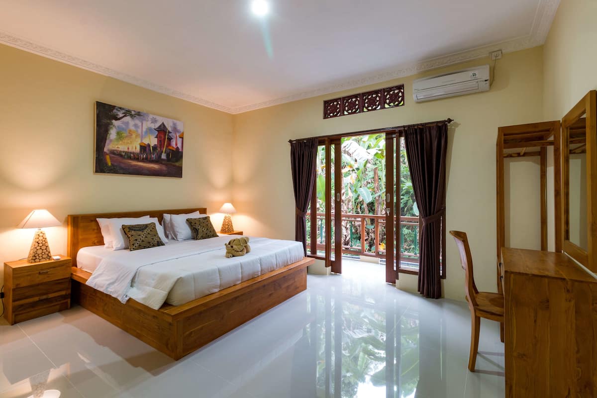 A bedroom with a wooden bed, nightstands, a desk, and a large window with curtains.