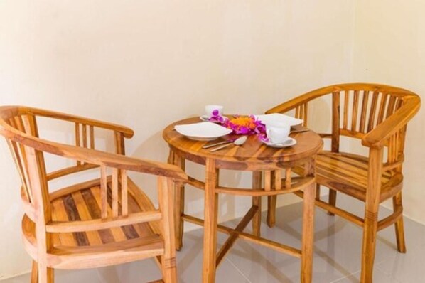 A wooden table with two chairs, a white plate, a cup, and a flower arrangement. - Alam Pangkung Ubud (Ubud)