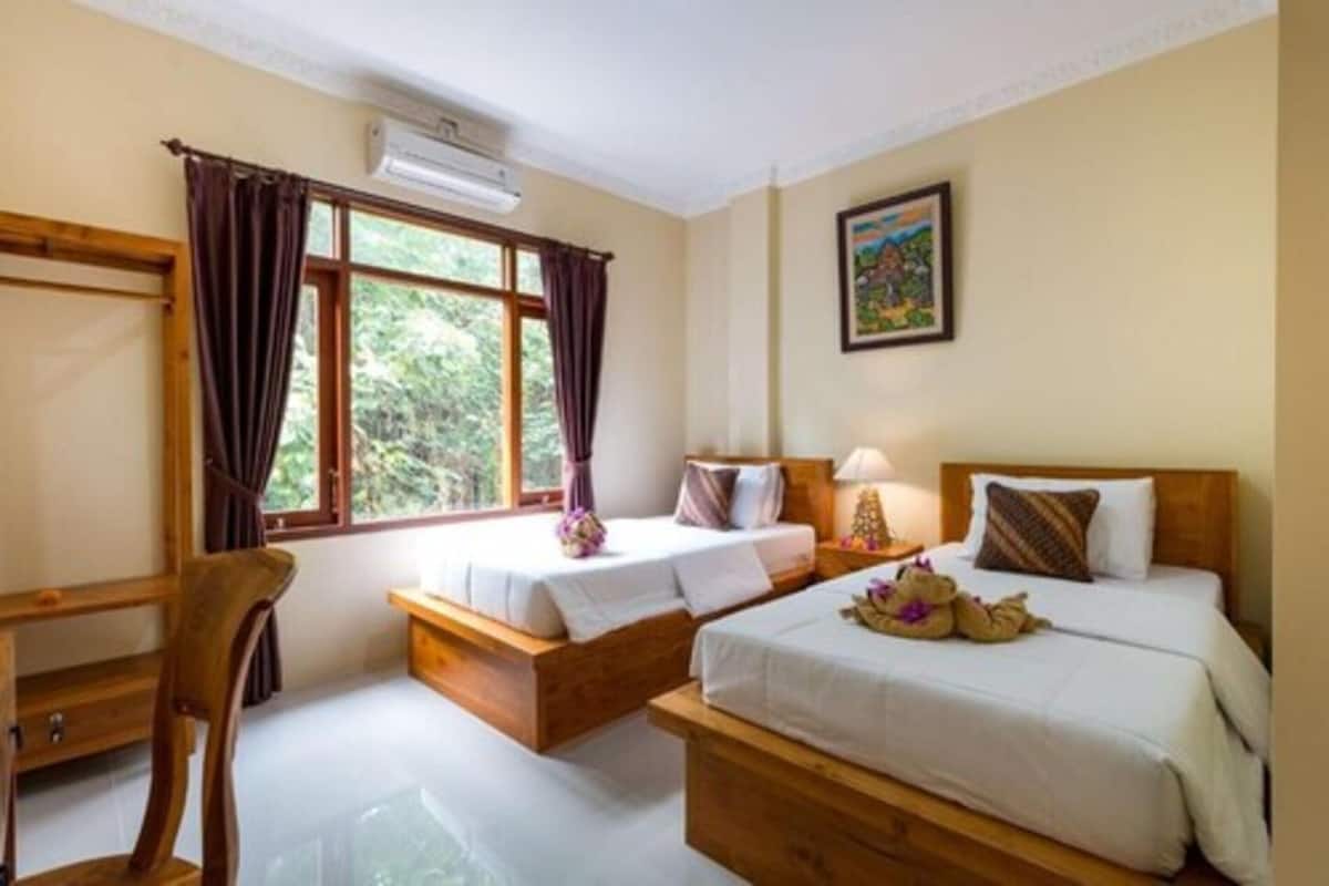 A room with two beds, a wooden desk, a chair, and a window with curtains.