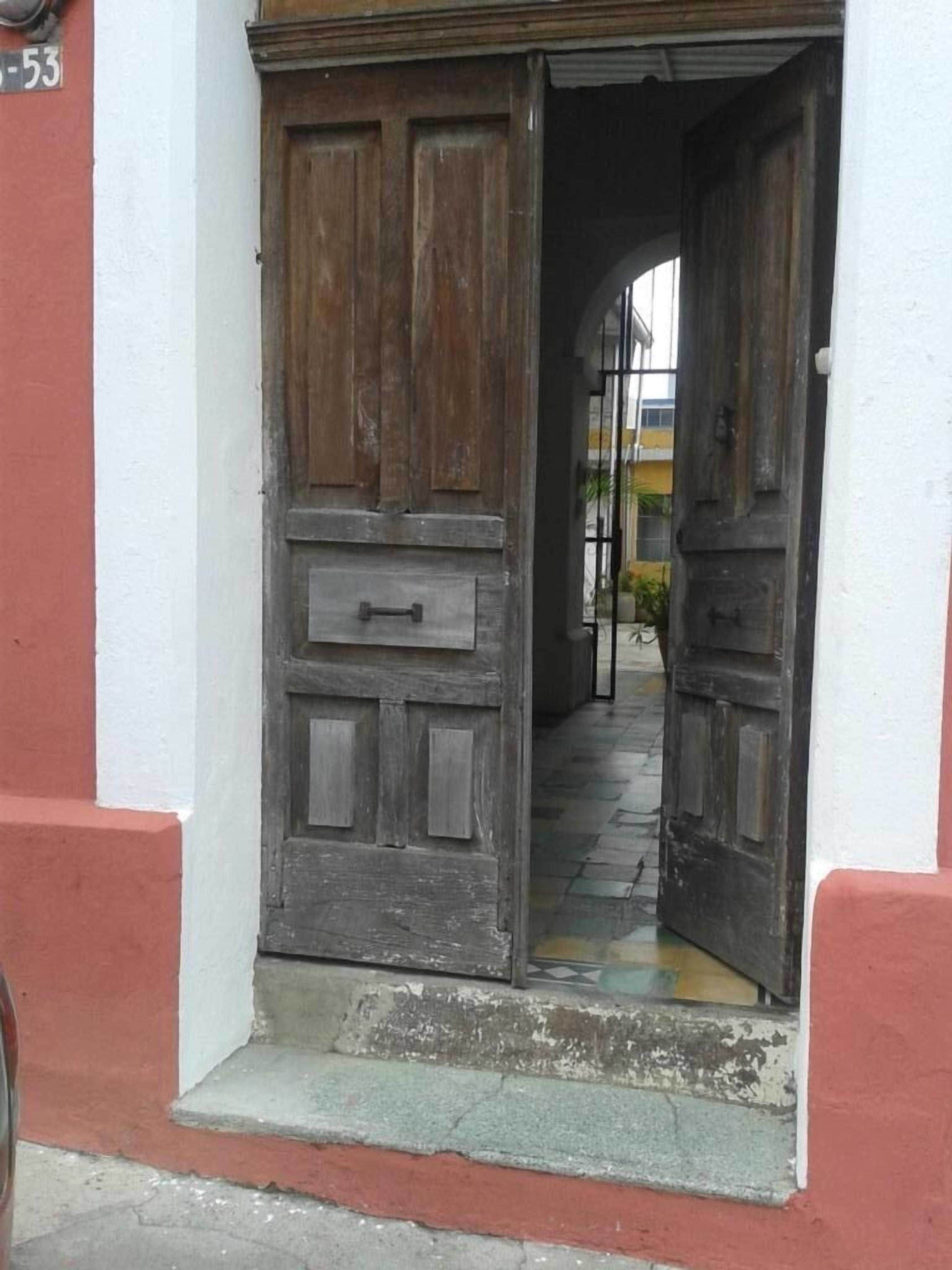 Une porte en bois rustique, dotée d’une poignée en métal, encadrée dans un mur aux couleurs blanche et rouge.