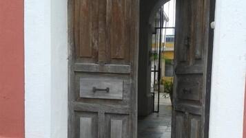 Une porte en bois rustique, dotée d’une poignée en métal, encadrée dans un mur aux couleurs blanche et rouge.