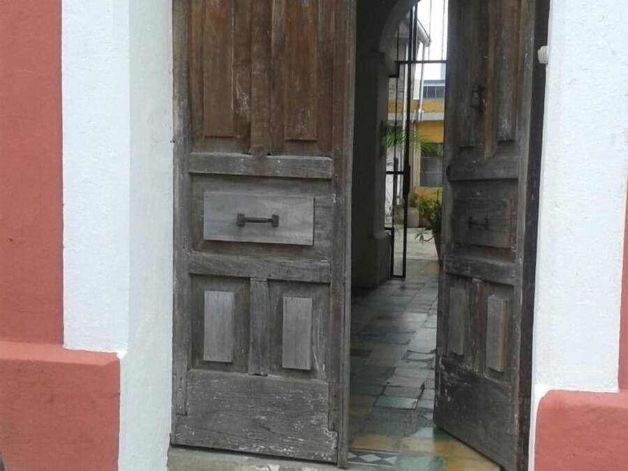 Une porte en bois rustique, dotée d’une poignée en métal, encadrée dans un mur aux couleurs blanche et rouge.