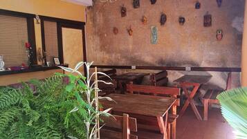 Un restaurante con mesas y bancos de madera, una pared decorada con varios adornos, y plantas en macetas.