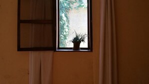 A room with a bed, a window with a view of greenery, and a potted plant on the windowsill.