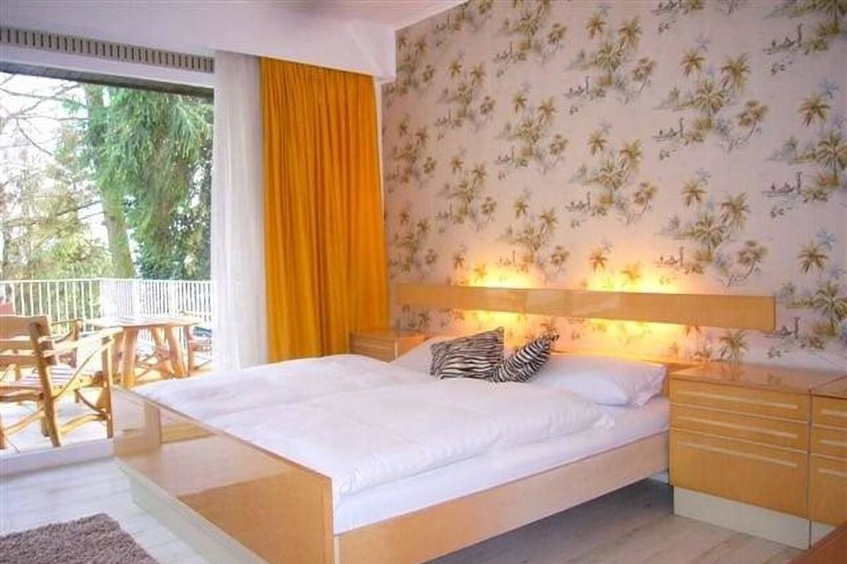 A bedroom with a bed, a nightstand, a dresser, and a window with curtains.