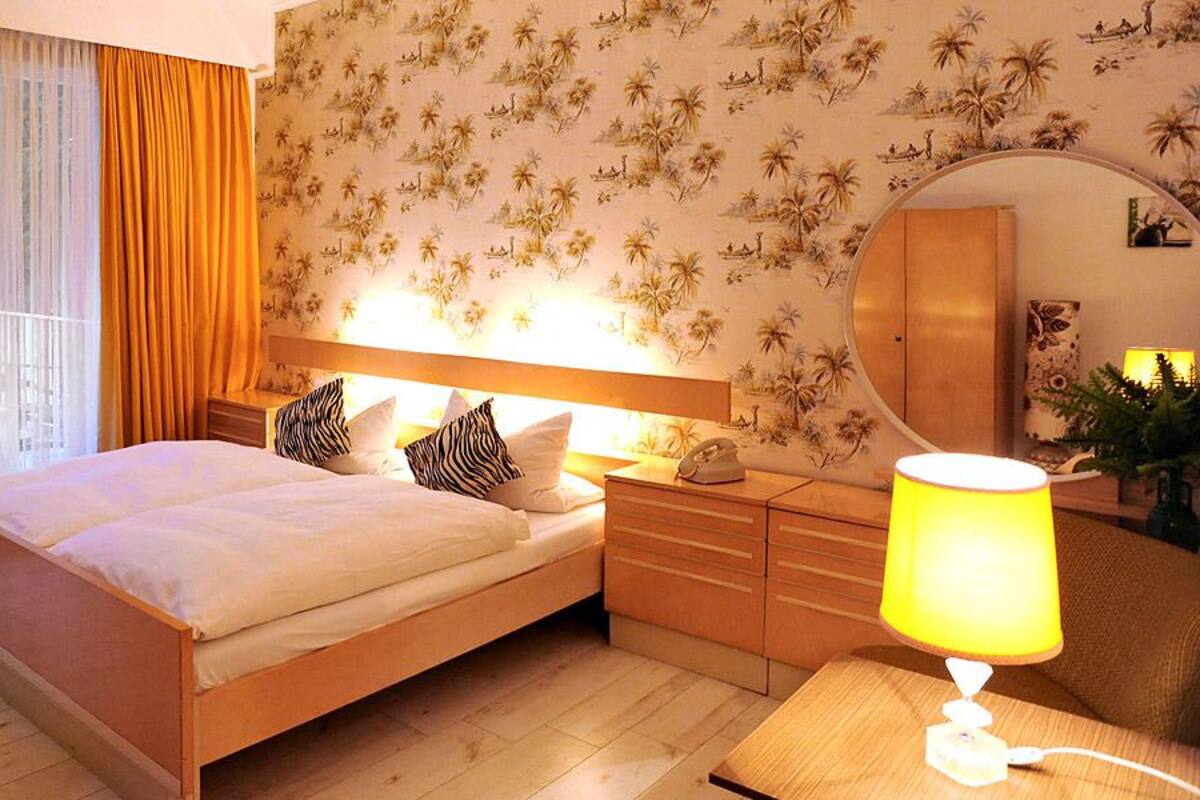 A bedroom with a bed, nightstands, a lamp, a mirror, and a view of the outdoors through a sliding door.