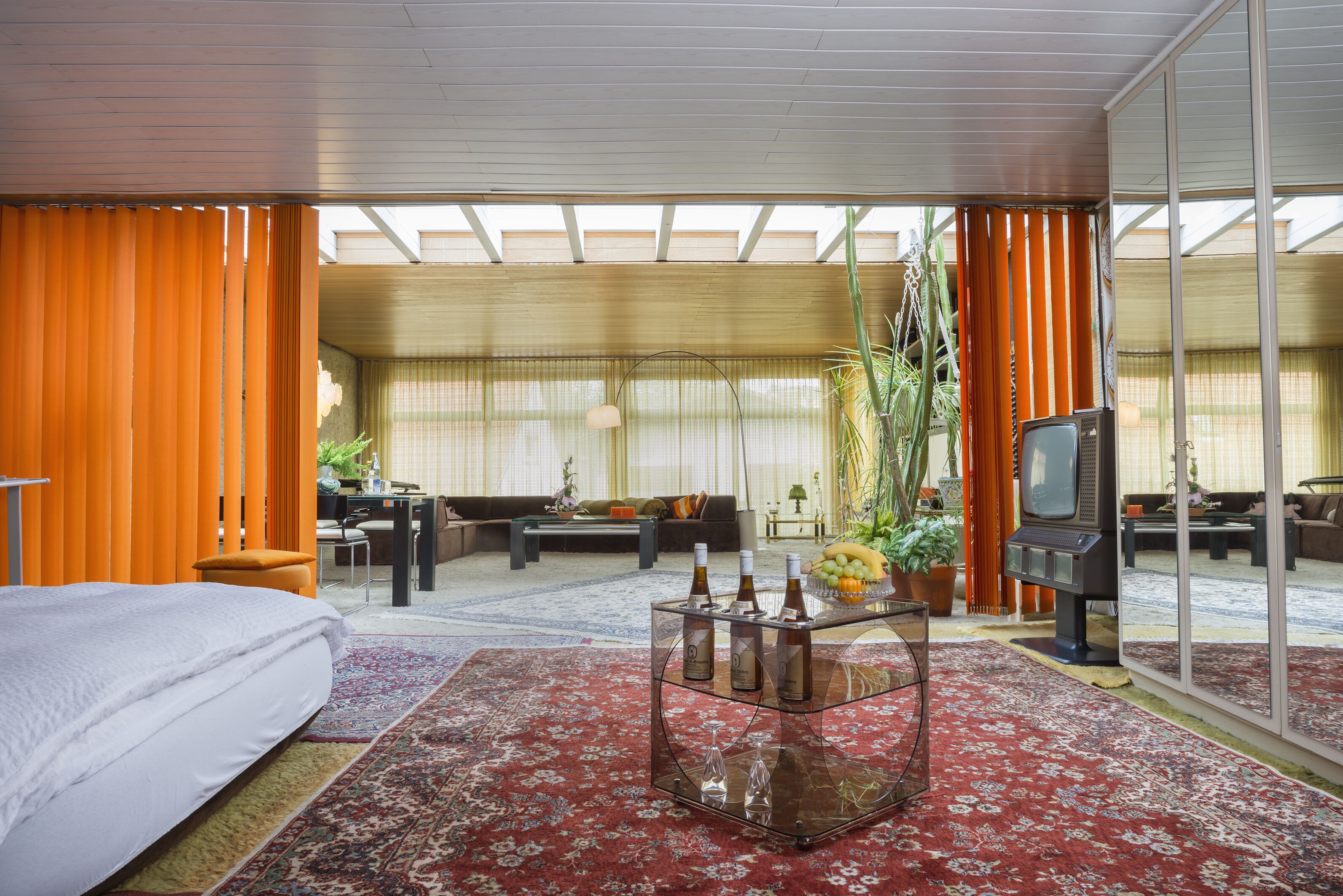 A hotel room with a bed, a glass coffee table with bottles, a sofa, and a television.